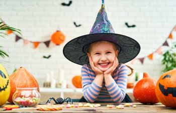 A girl in a witch hat surrounded by Halloween treats and decorations.
