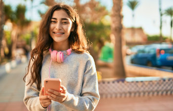 cheerful teenager with a pink phone in hand standing in the street, 