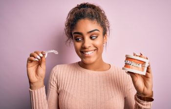 Young african american woman smiling happy holding professional orthodontic denture with metal braces and removable invisible aligner. Comparation of two dental straighten treatments
