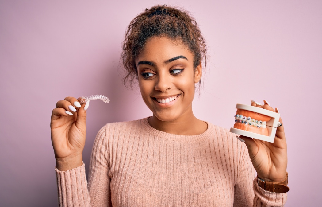 Young african american woman smiling happy holding professional orthodontic denture with metal braces and removable invisible aligner. Comparation of two dental straighten treatments, 