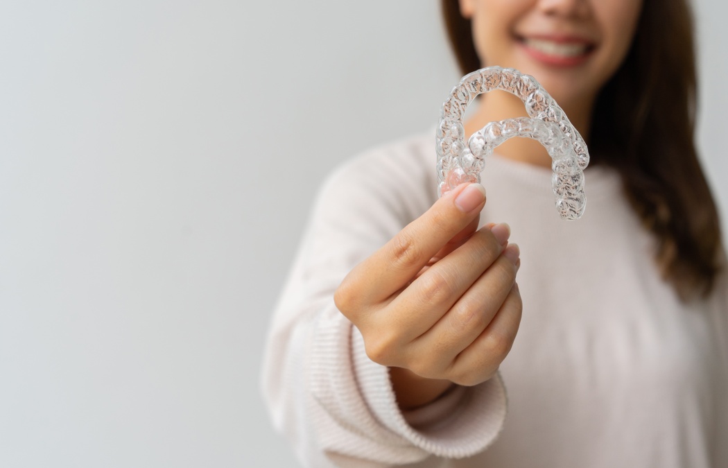 close up woman hand holding dental aligner retainer (invisible) on background for beautiful teeth and dental treatment course concept, 