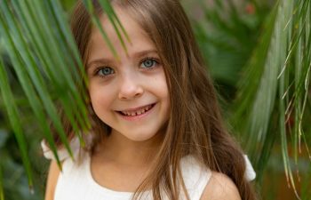The face of a little girl surrounded by tropical leaves. Closeup portrait of a beautiful child with perfect skin and dark hair. Natural cosmetics, health, cleanliness, skin care, beauty concept