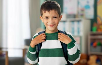 Child, face and laughing in school classroom or education with backpack for kindergarten, learning or joke. Boy, kid and portrait for study development on academy campus or student, humor or funny