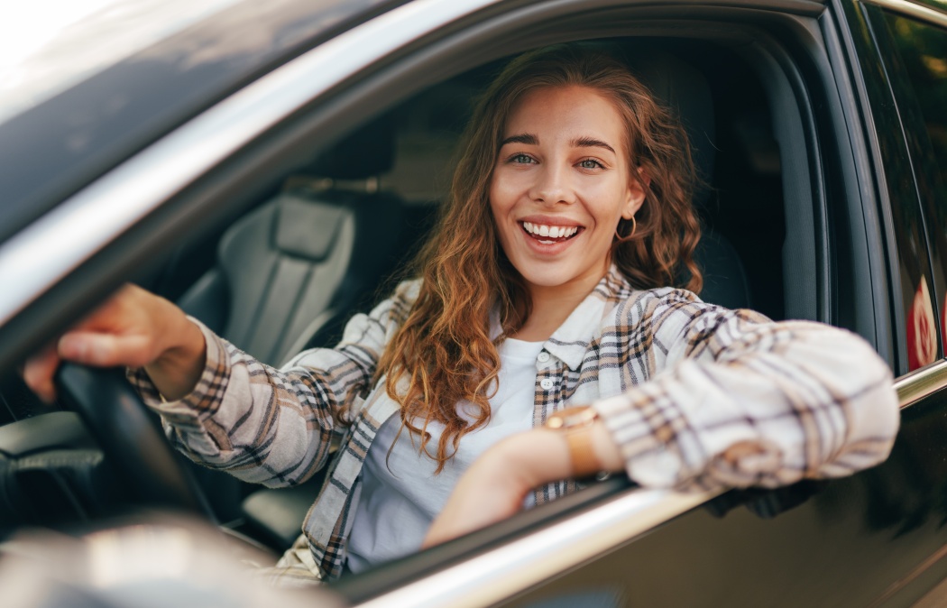 Happy smiling woman inside a car driving in the street, 