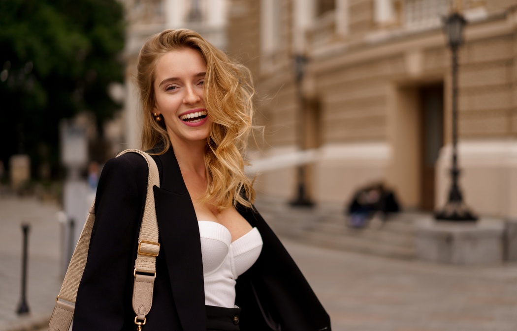 Beautiful smiling woman in elegant black suit posing outdoor in old european city. Blond wavy hairs, perfet skin., 